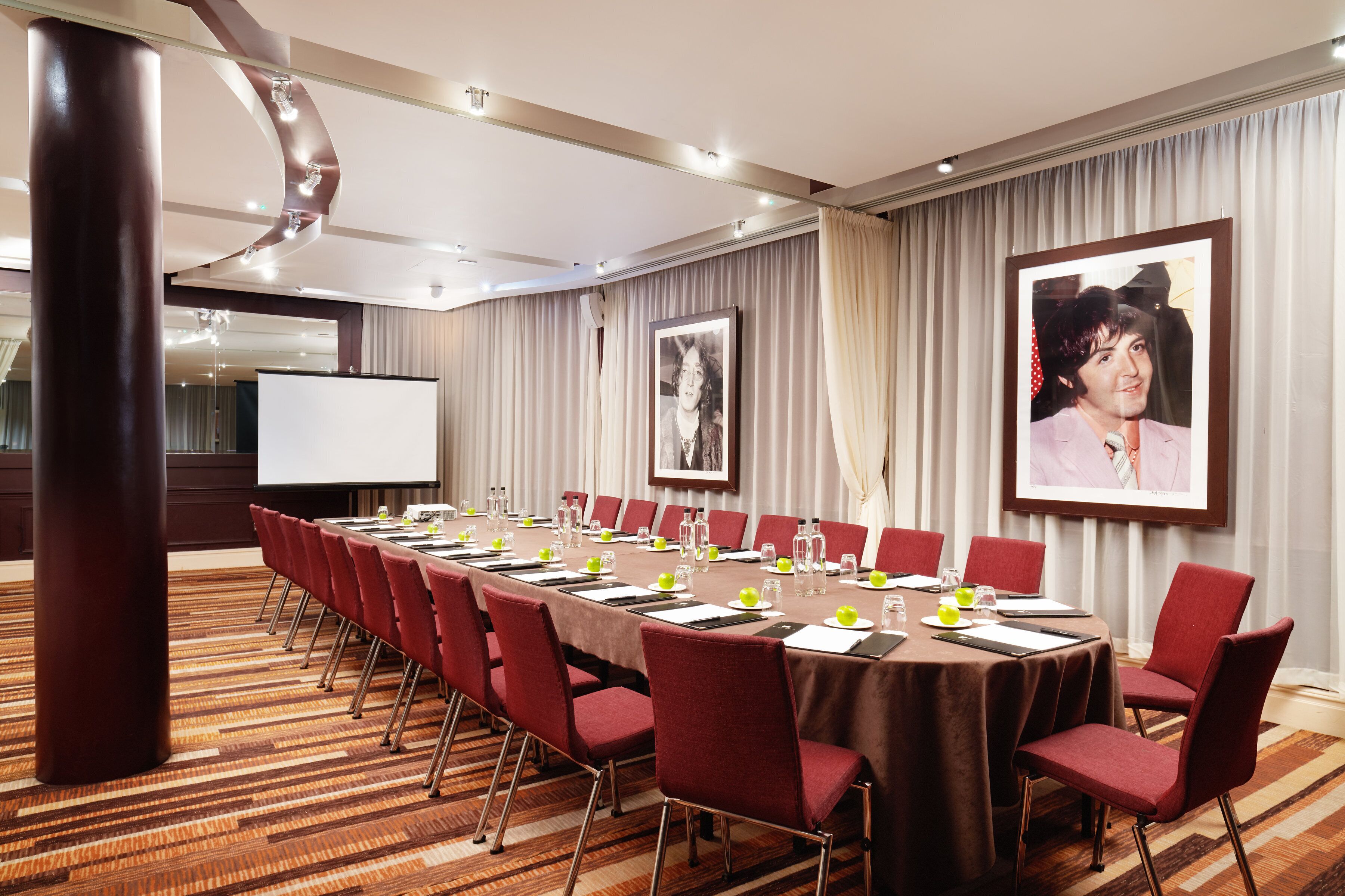 A conference room with a long table, red chairs, and a projector screen.
