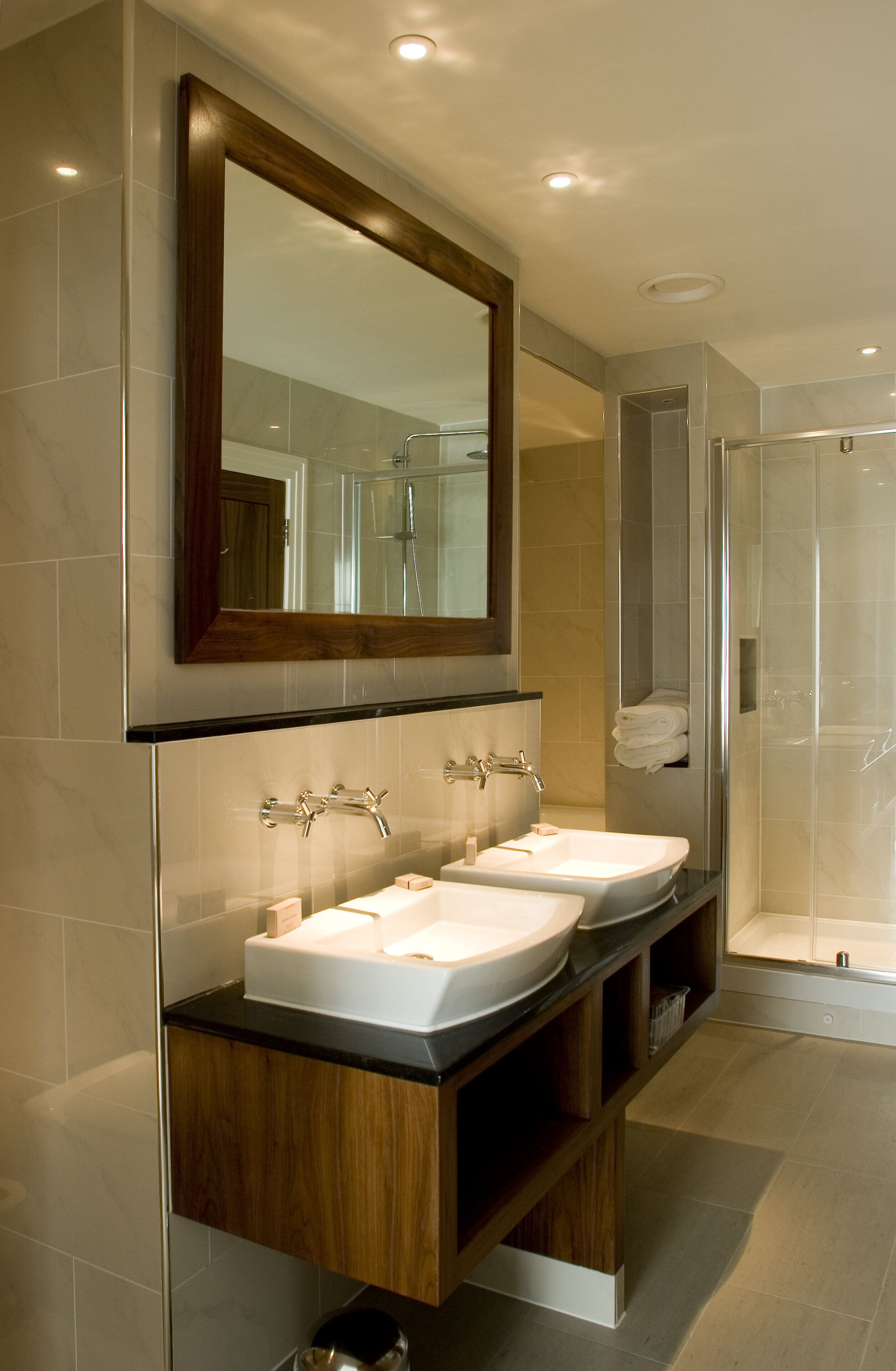 A modern bathroom with two sinks, a large mirror, and a walk-in shower.