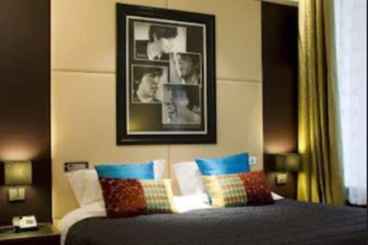 A hotel room with a large bed, a framed photo on the wall, and a nightstand with a lamp.