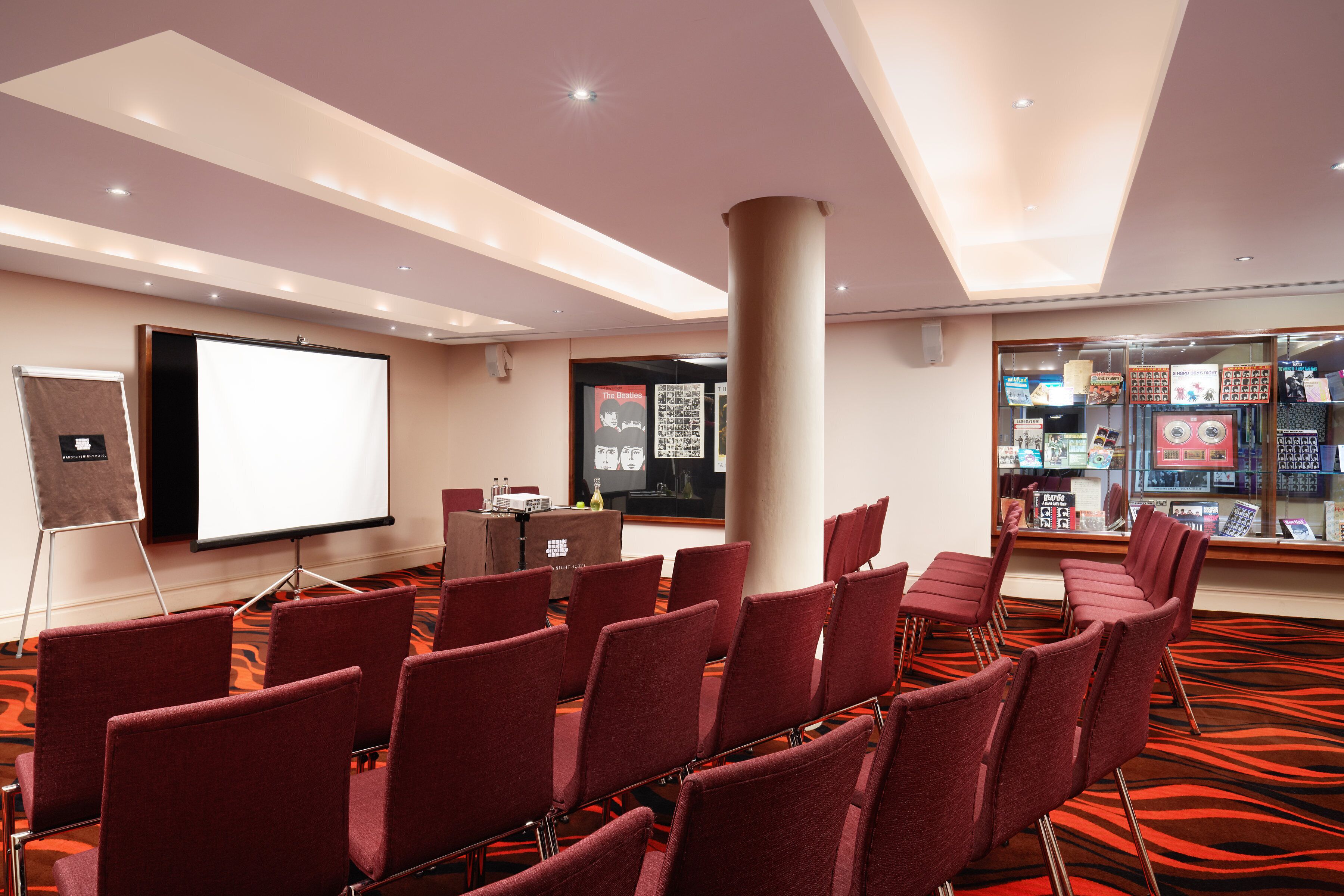 A conference room with rows of red chairs, a projection screen, and a large pillar.