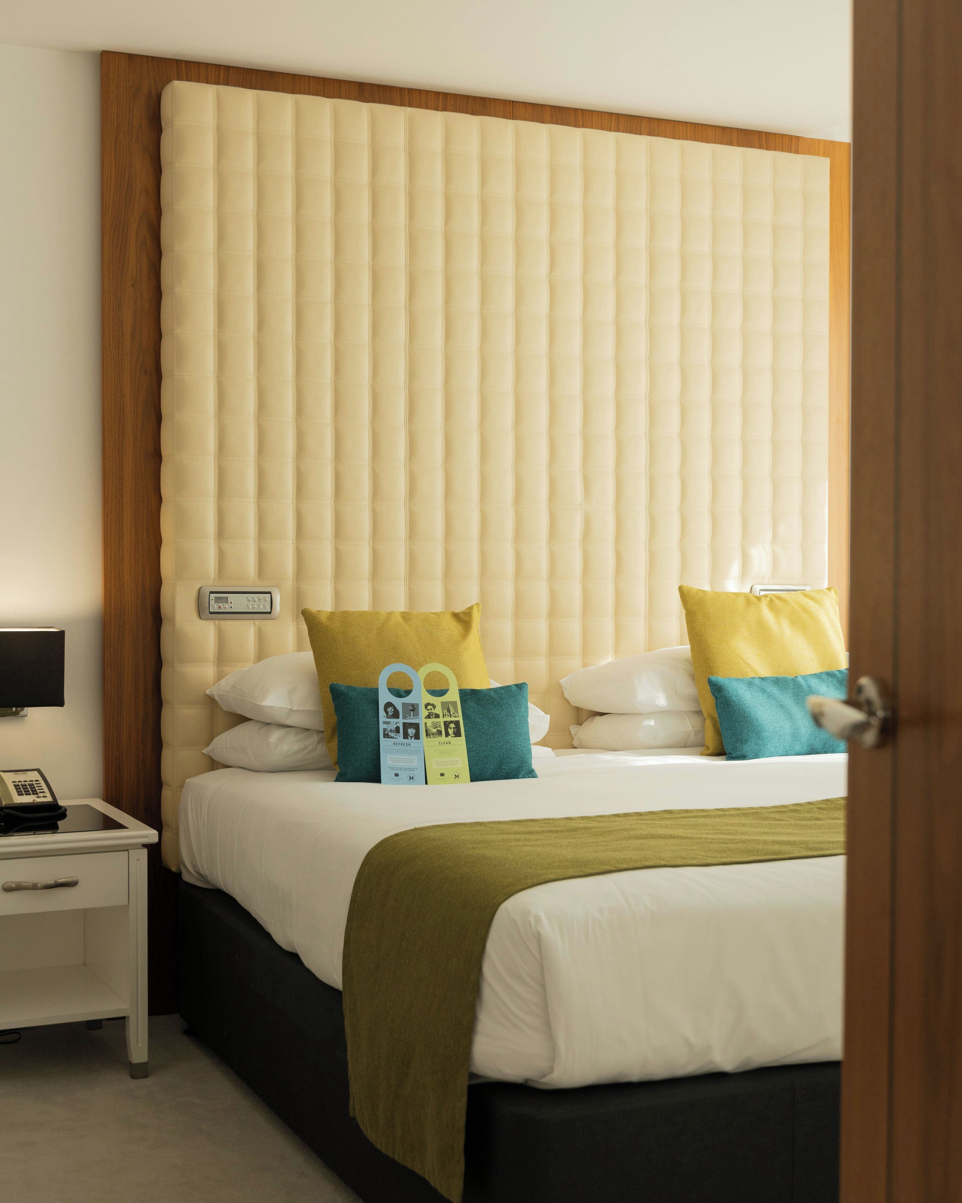 Habitación de hotel con cama, almohadas, mesita de noche con teléfono y termostato.