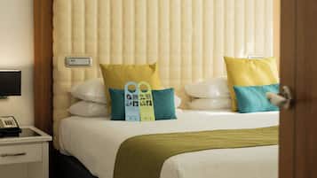 Habitación de hotel con cama, almohadas, mesita de noche con teléfono y termostato.