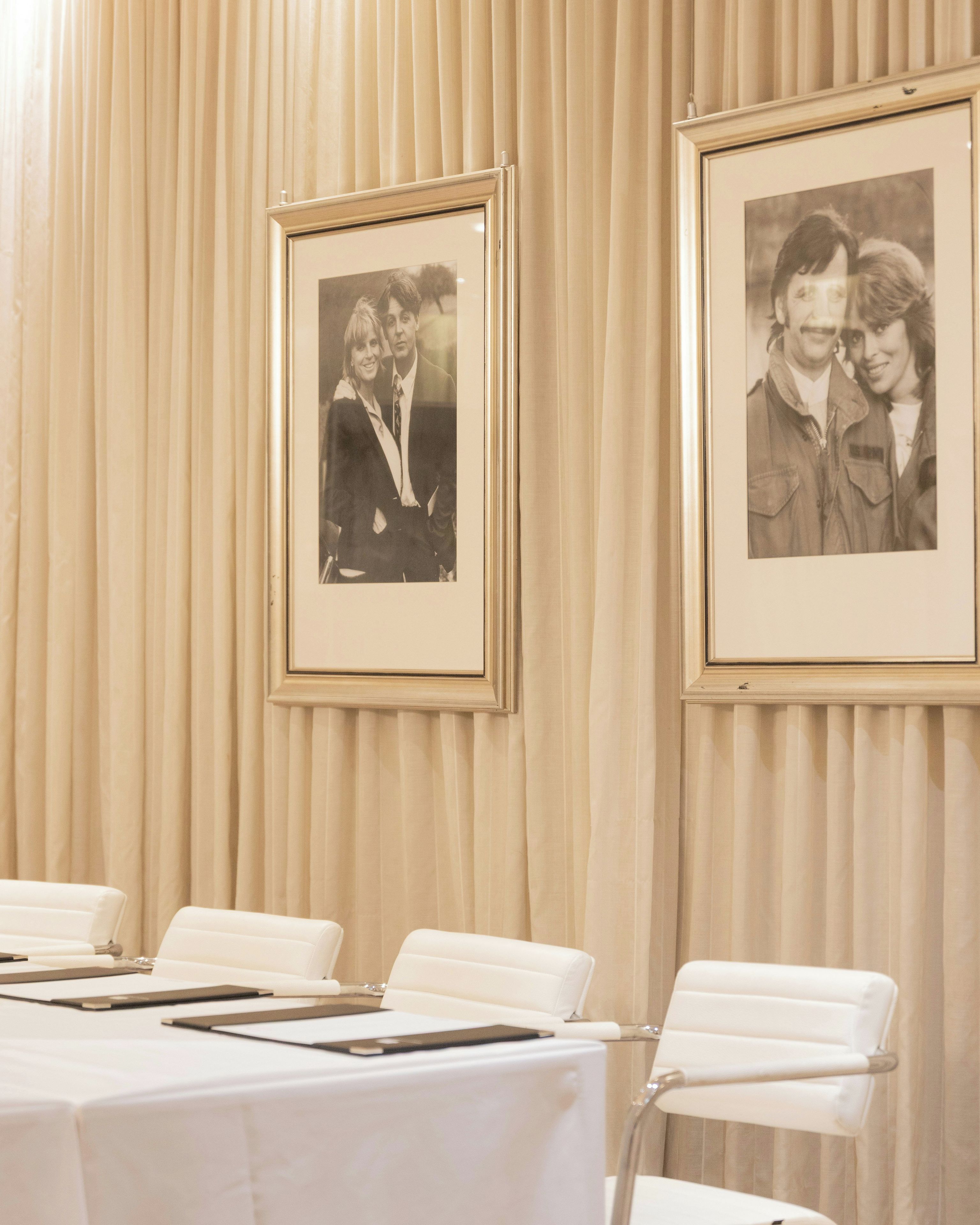 Un salón de conferencias con una mesa blanca, sillas y fotografías en blanco y negro enmarcadas en la pared.