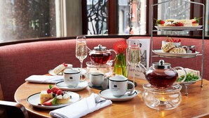 A table set with tea service, sandwiches, and desserts, with a view of the city through large windows. - Hard Days Night Hotel Liverpool (Liverpool)