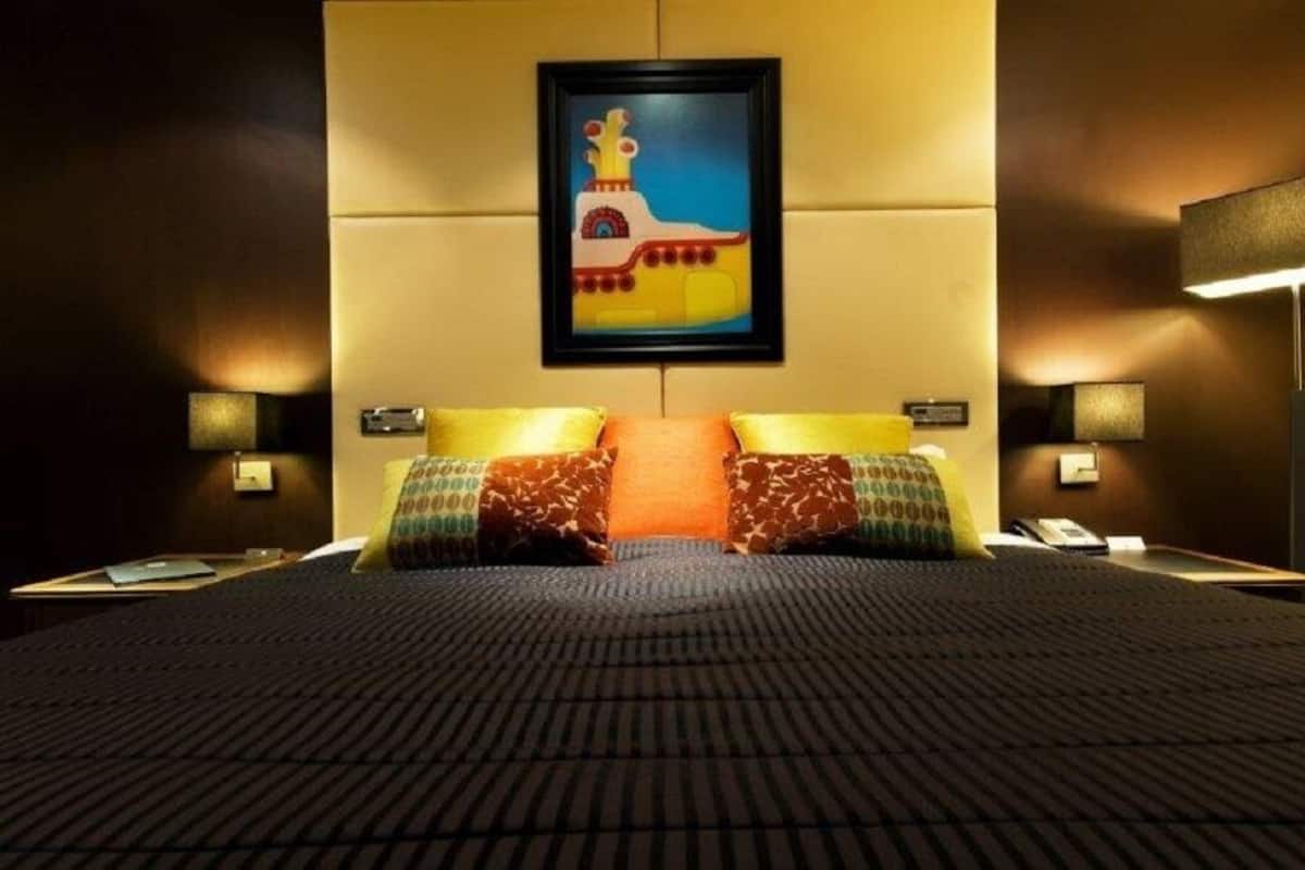 A hotel room with a large bed, two bedside tables, a nightstand, a framed picture on the wall, and two wall-mounted lamps.