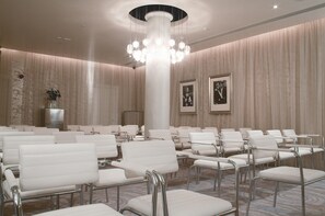 A conference room with rows of white chairs, a central pillar, and a chandelier.