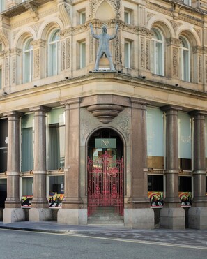 A building with a classical architectural style, featuring a prominent statue above the entrance, large windows, and a red gate.