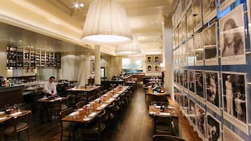 Un restaurante con largas mesas de madera, lámparas colgantes y una zona de bar con estantes llenos de botellas.