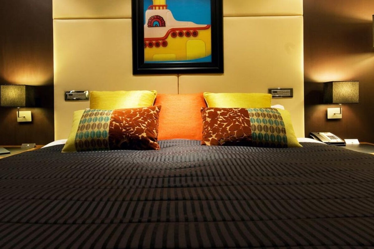 A hotel room with a large bed, two bedside lamps, a nightstand with a phone, and a painting on the wall.