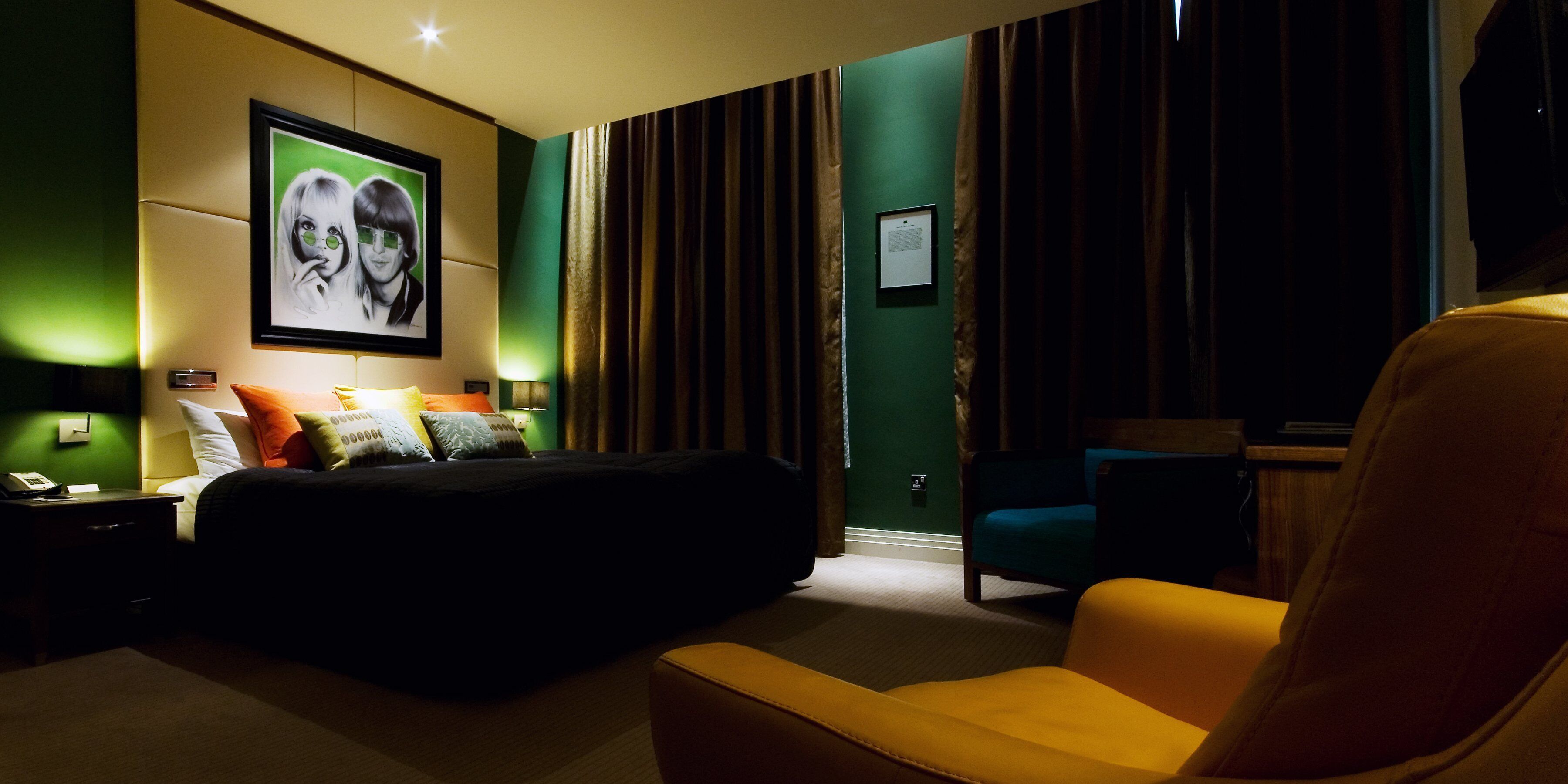 A hotel room with a bed, a chair, a nightstand, and a wall-mounted picture.