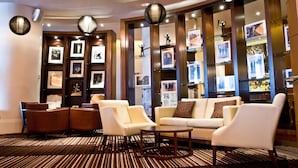 A lobby with a sofa, chairs, a coffee table, framed pictures, and a bar area. - Hard Days Night Hotel Liverpool (Liverpool)