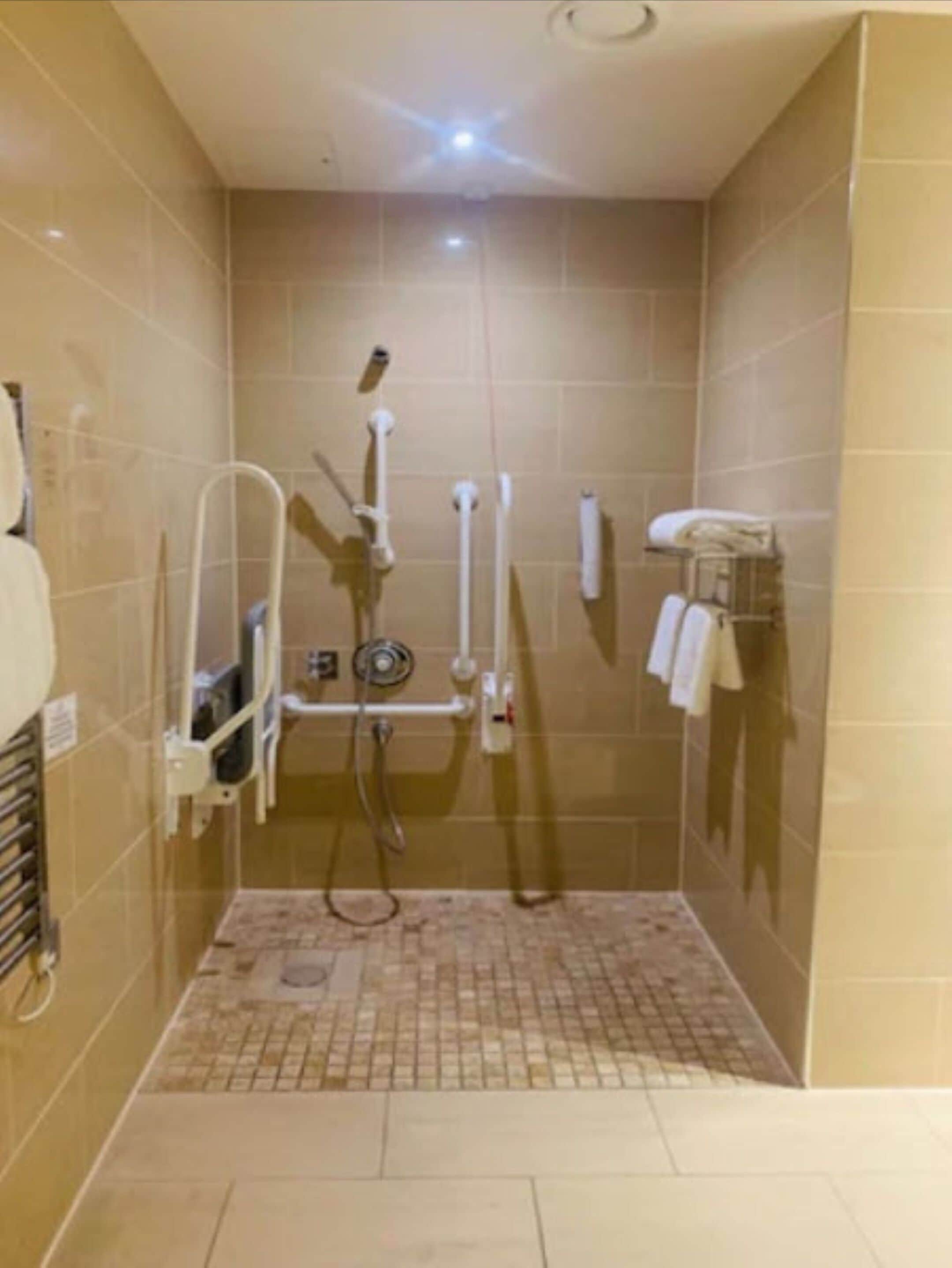 Un pequeño box de ducha con azulejos, un cabezal de ducha manual y un perchero para toallas.