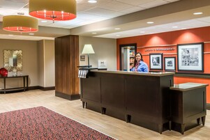 A hotel reception area with a dark reception desk, a red carpet, and framed pictures on the wall.