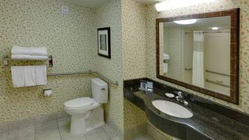 A bathroom with a toilet, sink, and mirror. There are towels on a rack and a framed picture on the wall.