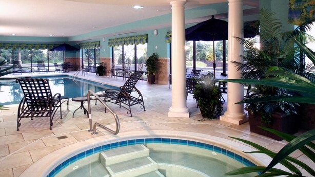 An indoor swimming pool with steps leading into it, surrounded by lounge chairs and potted plants.