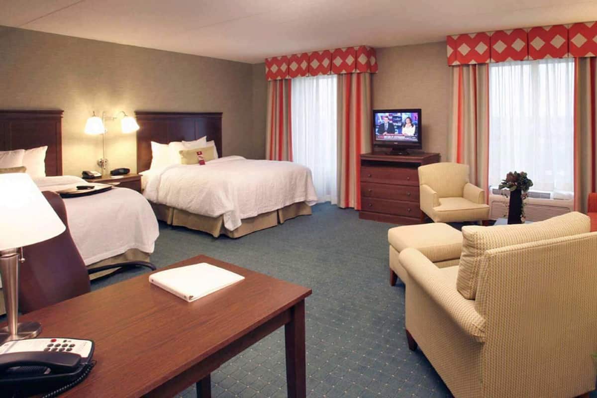 A hotel room with two beds, a TV, a desk with a phone, a chair, a sofa, and a small table.