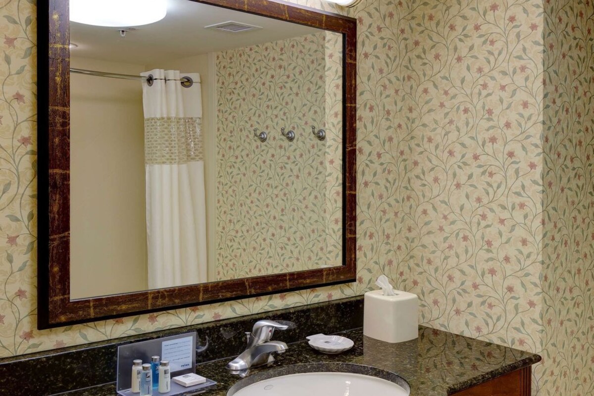 A bathroom with a marble sink, a large mirror, and a towel rack with folded towels.