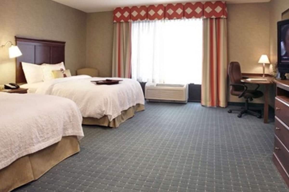 Une chambre d’hôtel avec deux lits, un bureau, une chaise, une télévision et une fenêtre avec des rideaux.