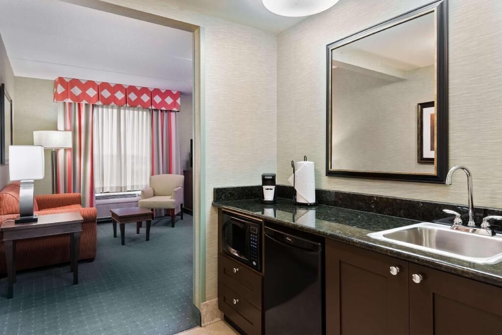 A hotel room with a kitchenette, a dining area, a large mirror, and a view of the room.