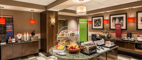 A hotel breakfast area with a buffet counter, various food items, and a coffee station.