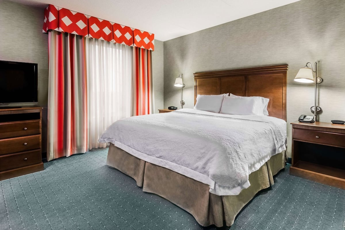 A hotel room with a bed, a TV, a desk with a lamp, and a telephone.