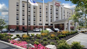 A Hampton Inn hotel with a parking lot, a flag, and a landscaped garden with flowers.