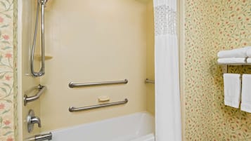 A bathroom with a bathtub, shower, and handrails.