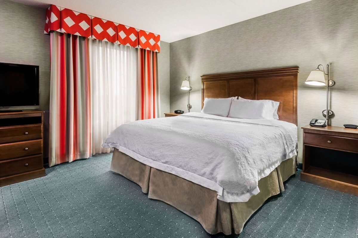 A hotel room with a bed, a TV, a desk with a lamp, and a telephone.