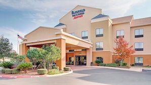 A Fairfield Inn & Suites by Marriott hotel with a covered entrance, a flag, and landscaped greenery. - Fairfield Inn & Suites by Marriott San Antonio Seaworld (San Antonio)