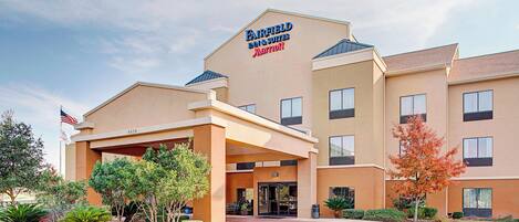 A Fairfield Inn & Suites by Marriott hotel with a covered entrance, a flag, and landscaped greenery.