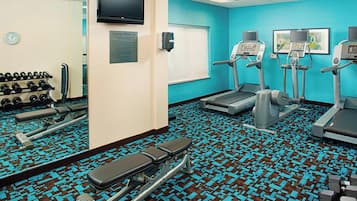 A gym with exercise equipment, a clock, and a sign indicating room use.