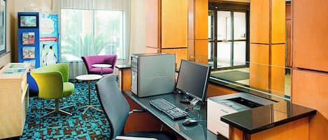 A hotel room with a desk, computer, chairs, and a large window.
