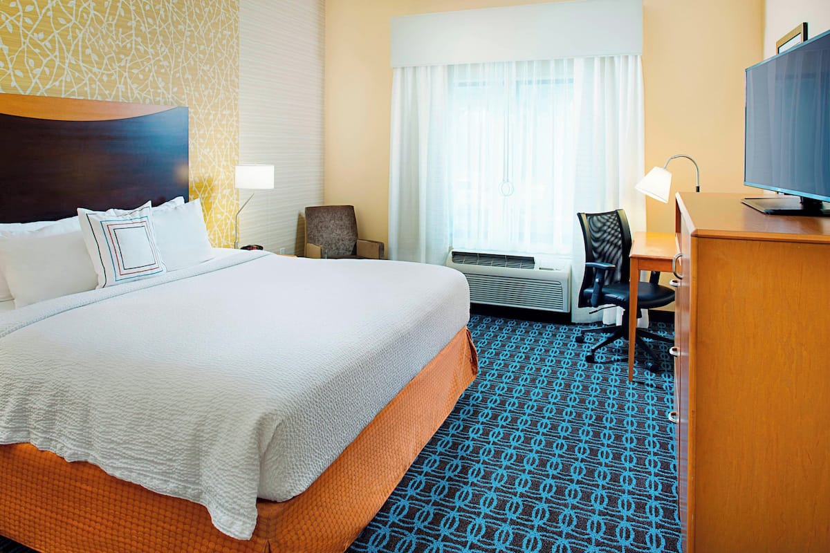 Ein Hotelzimmer mit einem großen Bett, einem Schreibtisch mit Computer, einem Stuhl und einem Fernseher.