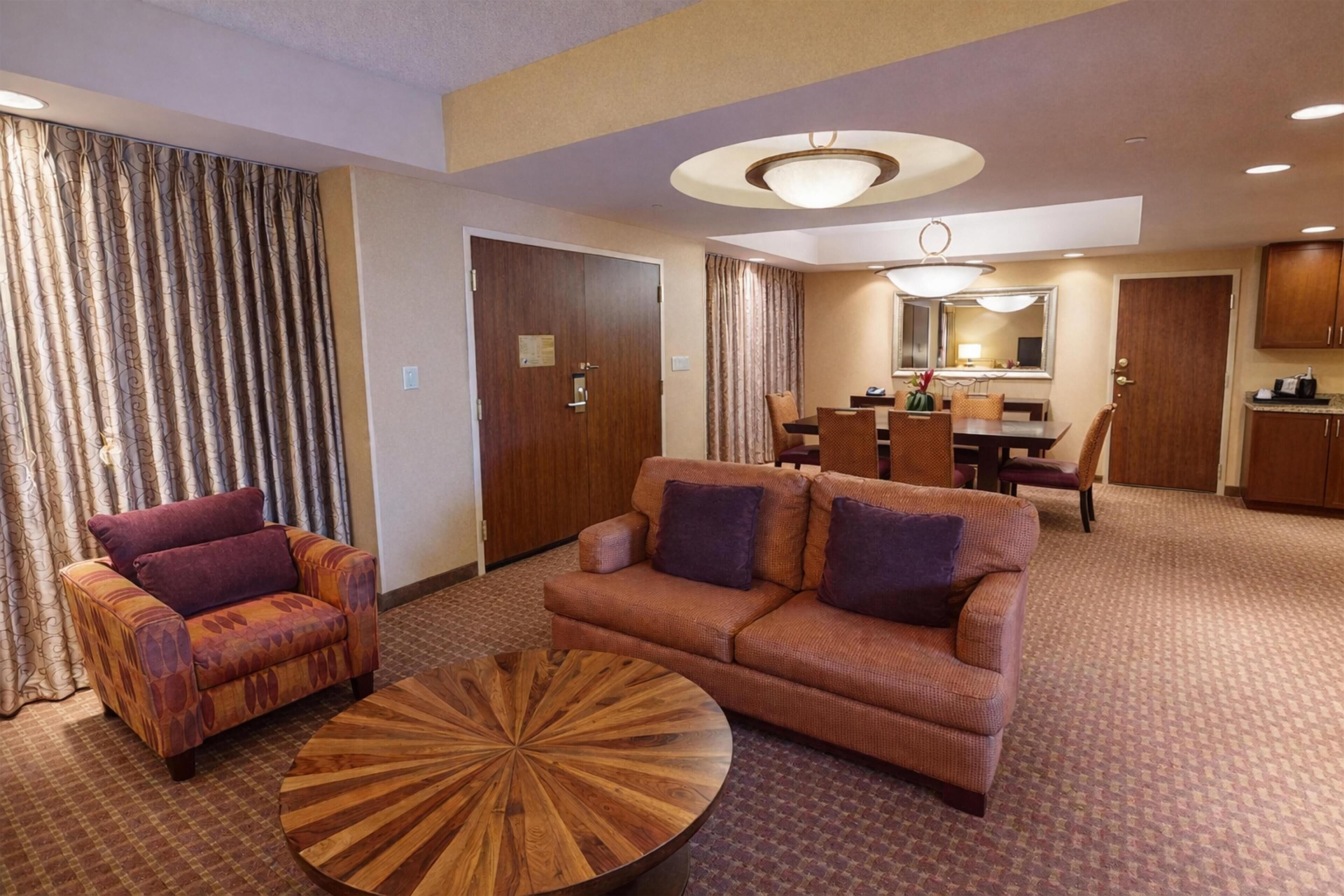Ein Hotelzimmer mit einer Couch, einem Sessel, einem Esstisch und einem runden Couchtisch.