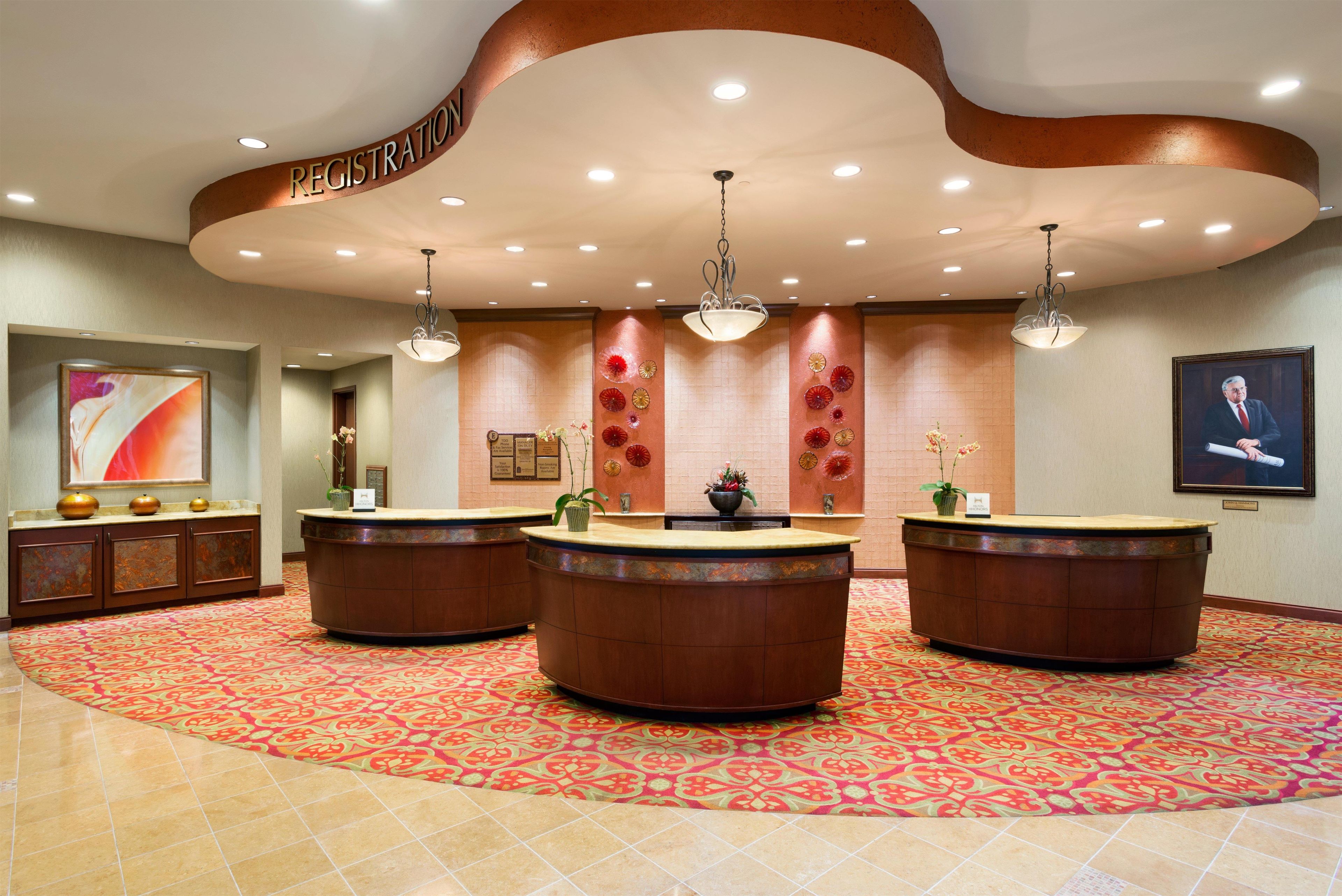 A hotel reception area with a registration desk, multiple light fixtures, and a patterned carpet.