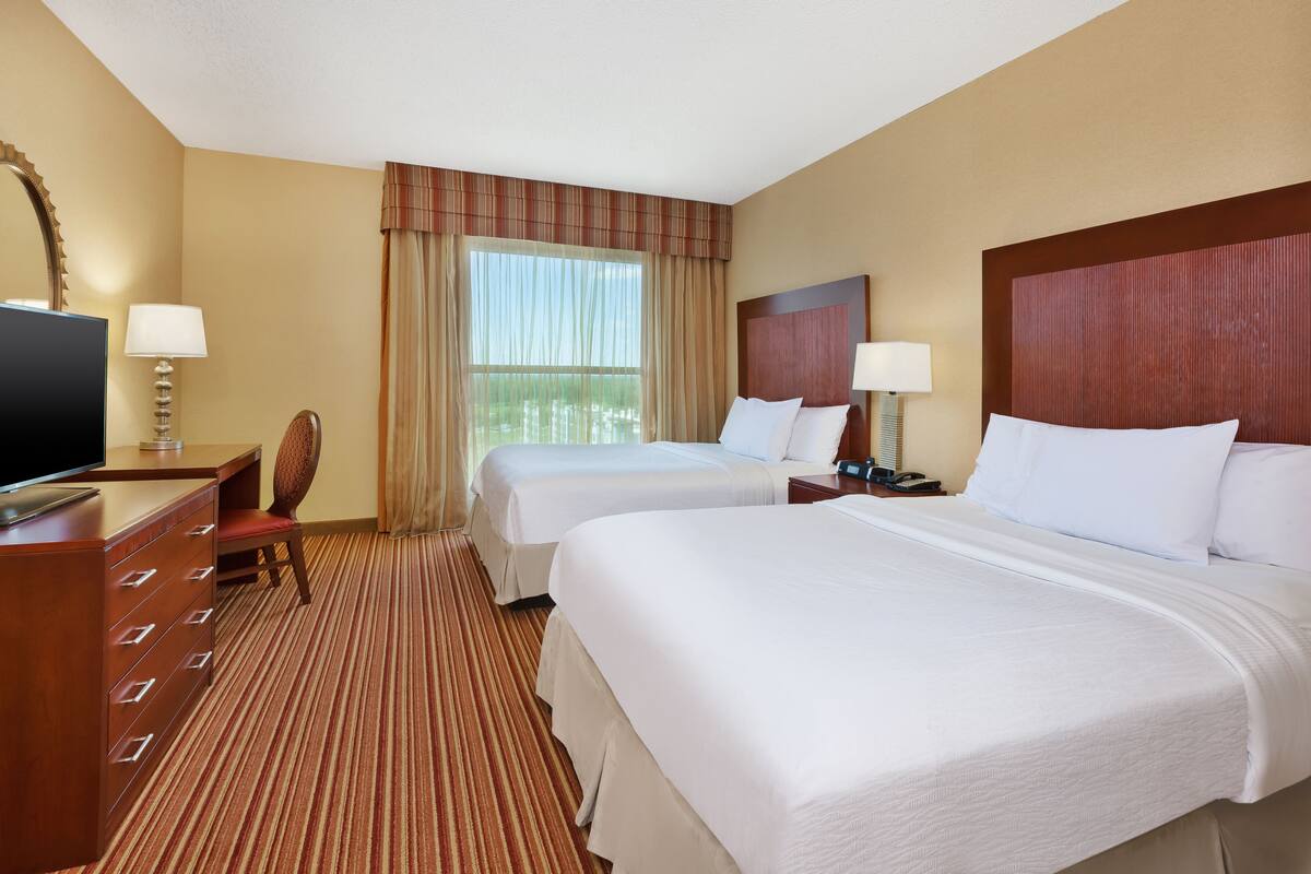 A hotel room with two beds, a desk, a chair, a TV, and a window with curtains.