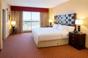 A hotel room with a large bed, two bedside tables with lamps, a view of the city through the window, and a red accent wall. - Embassy Suites by Hilton Norman Hotel & Conference Center (Norman)
