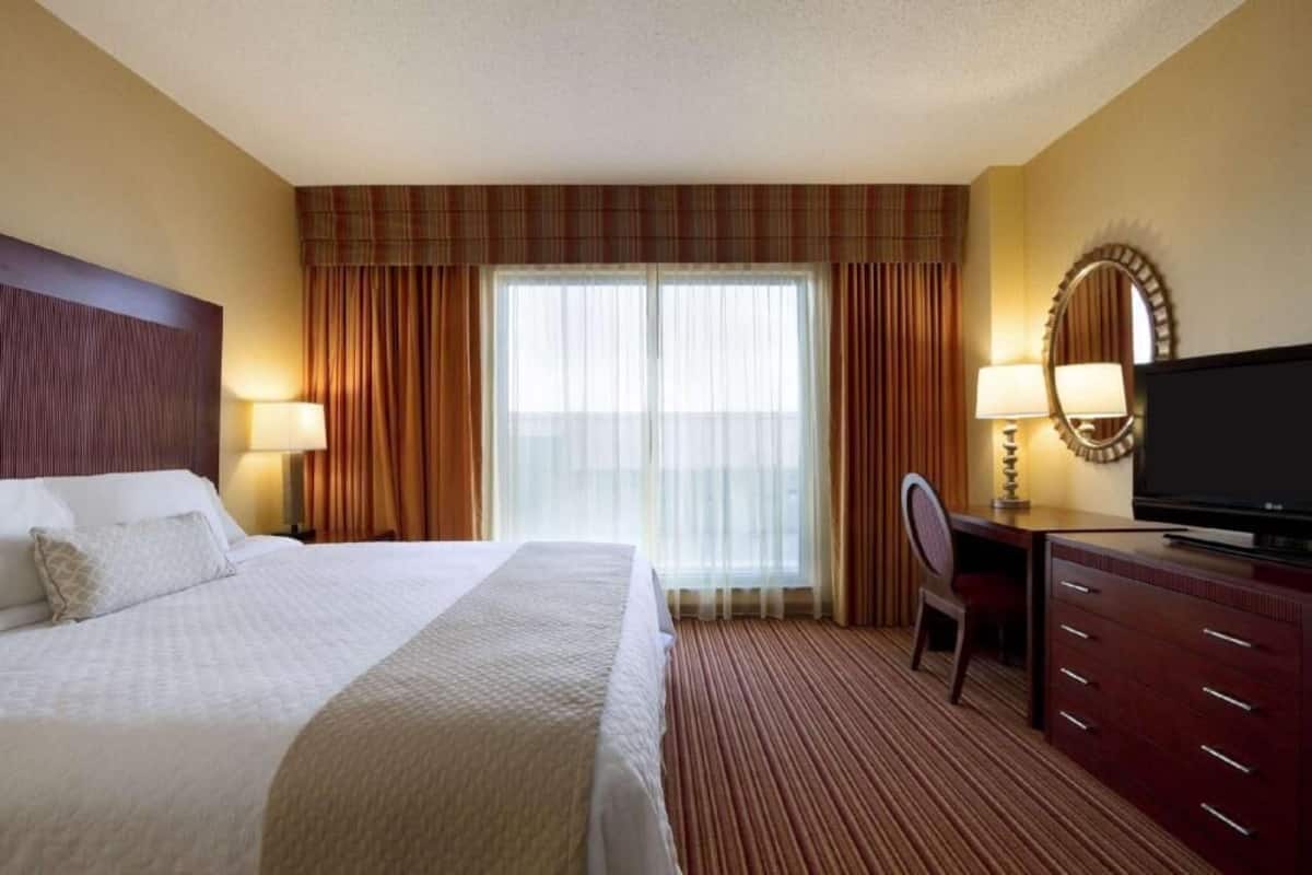 A hotel room with a bed, a desk, a television, a chair, and a window with curtains.