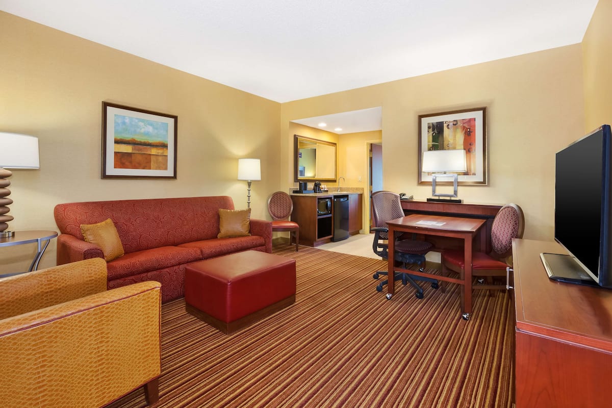 A hotel room with a red sofa, a wooden desk, a television, and a dining area.