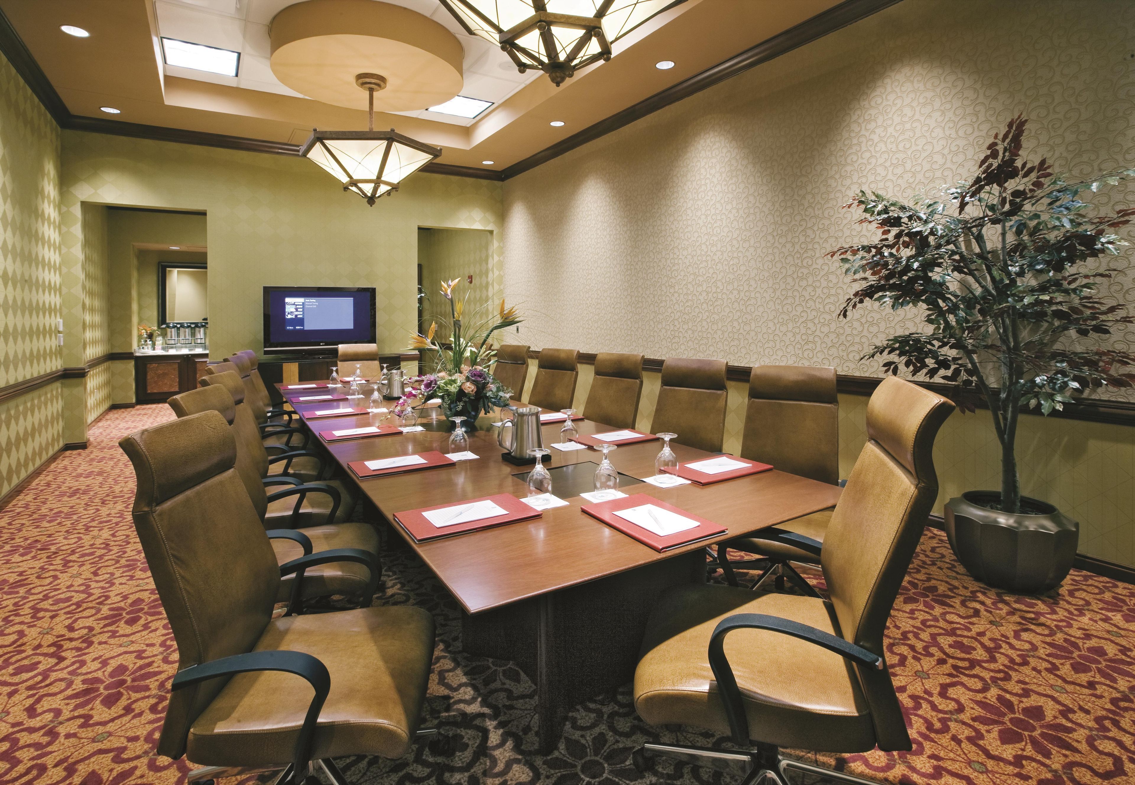 A conference room with a long table, chairs, a television, and a potted plant.