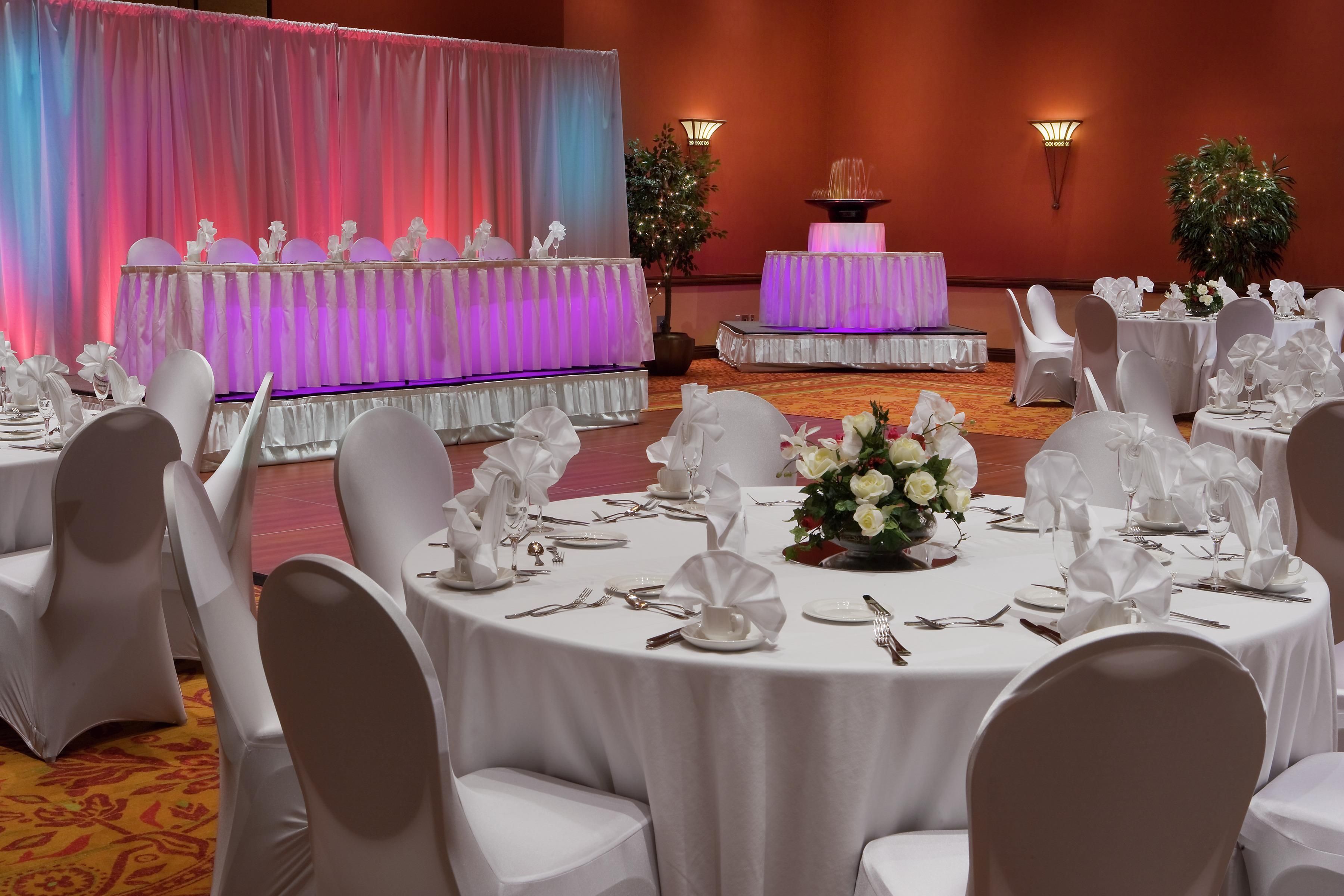 Un salón de banquetes con mesas redondas dispuestas para un evento formal, con manteles blancos, sillas y centros de mesa florales.