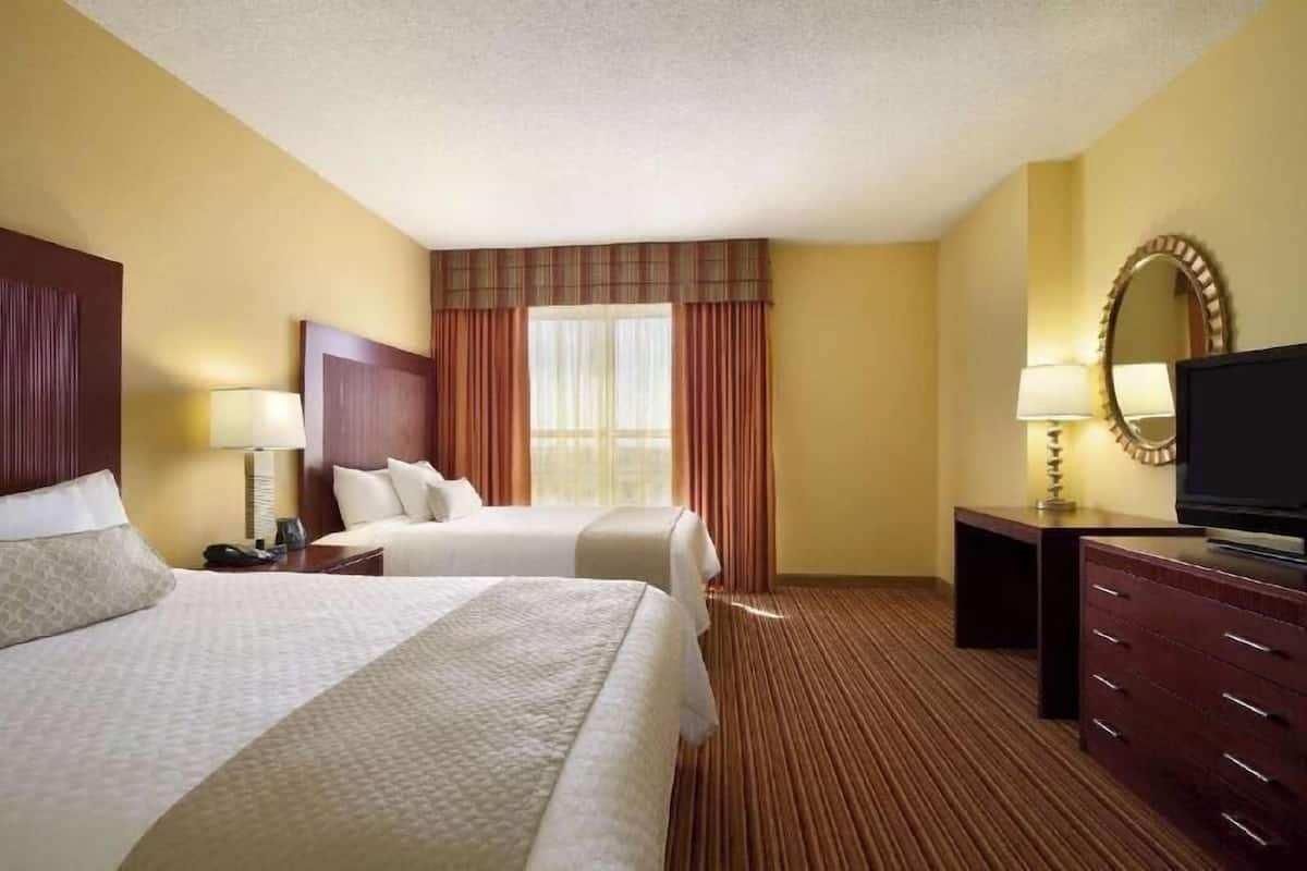 A hotel room with two beds, a television, a desk with a lamp, and a large mirror.