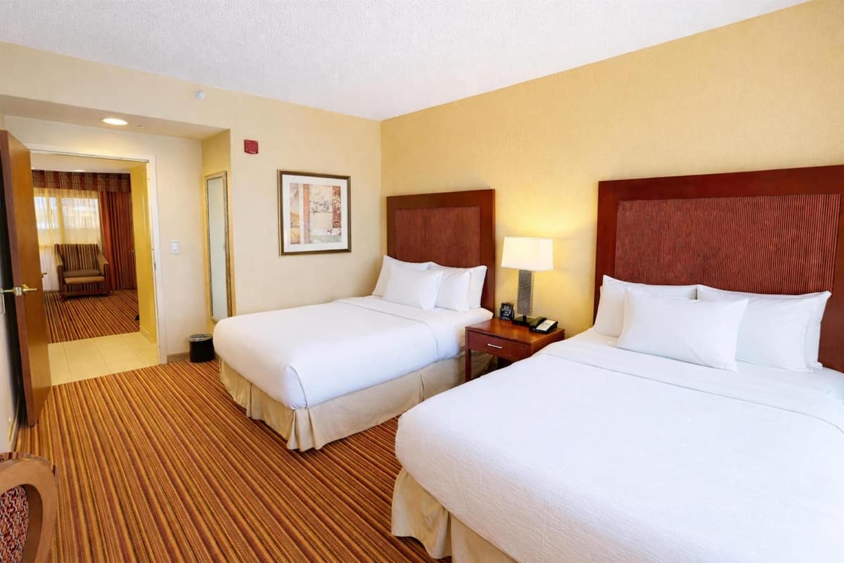 A hotel room with two beds, a wooden headboard, a nightstand with a lamp, and a framed picture on the wall.