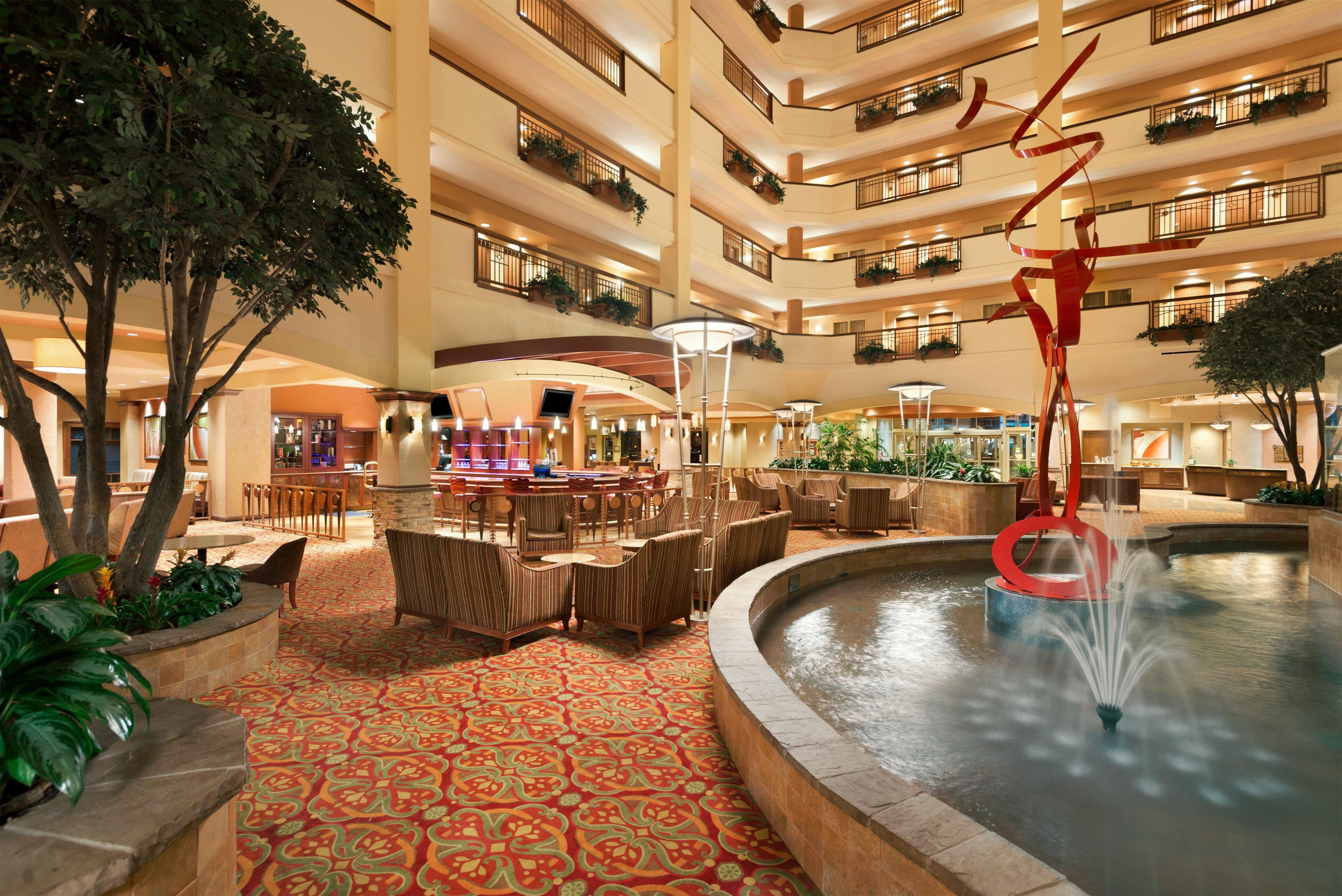 A multi-level hotel lobby with a central fountain, seating areas, and a bar/lounge.