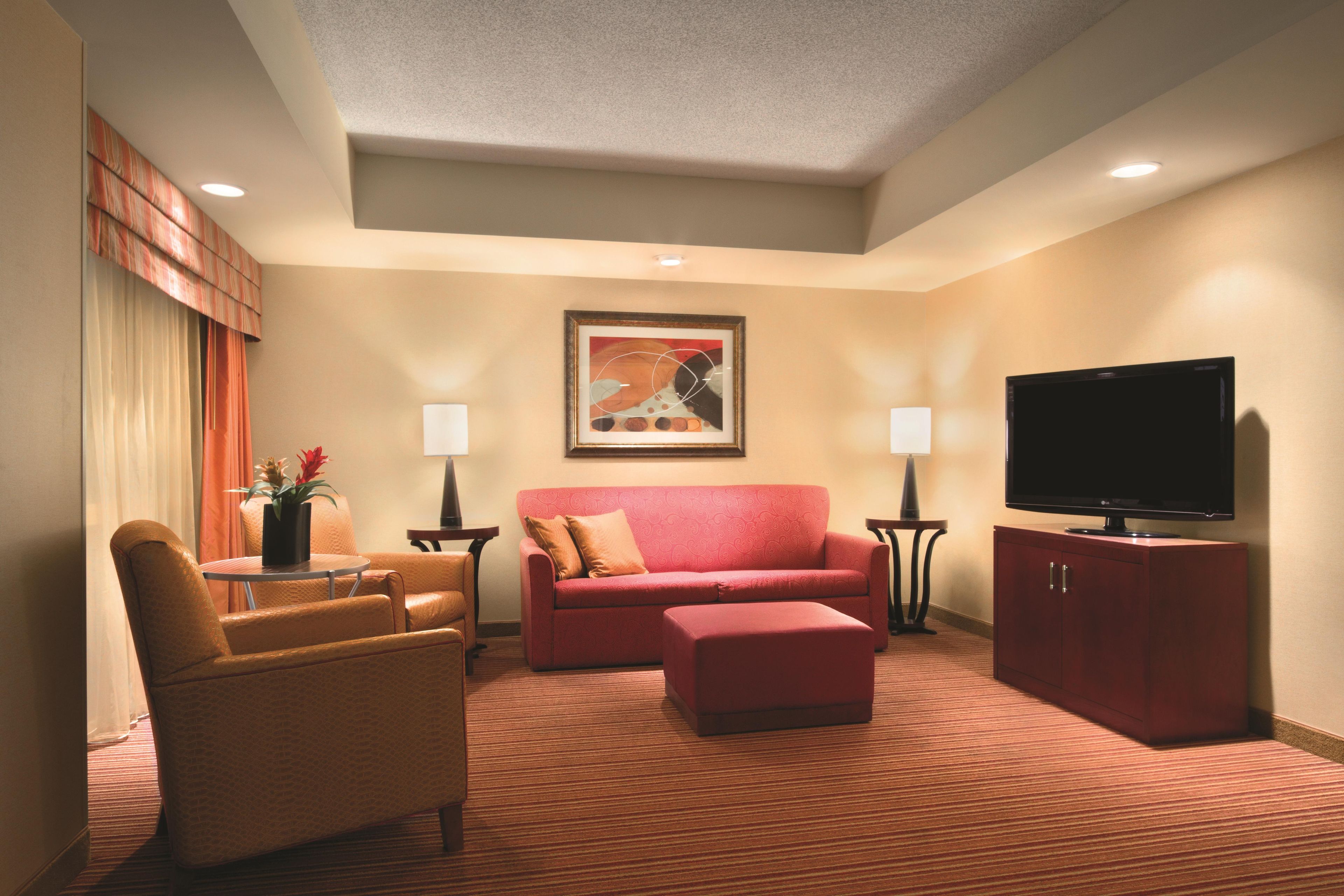 A hotel room with a red sofa, a brown armchair, a television, and a painting on the wall.