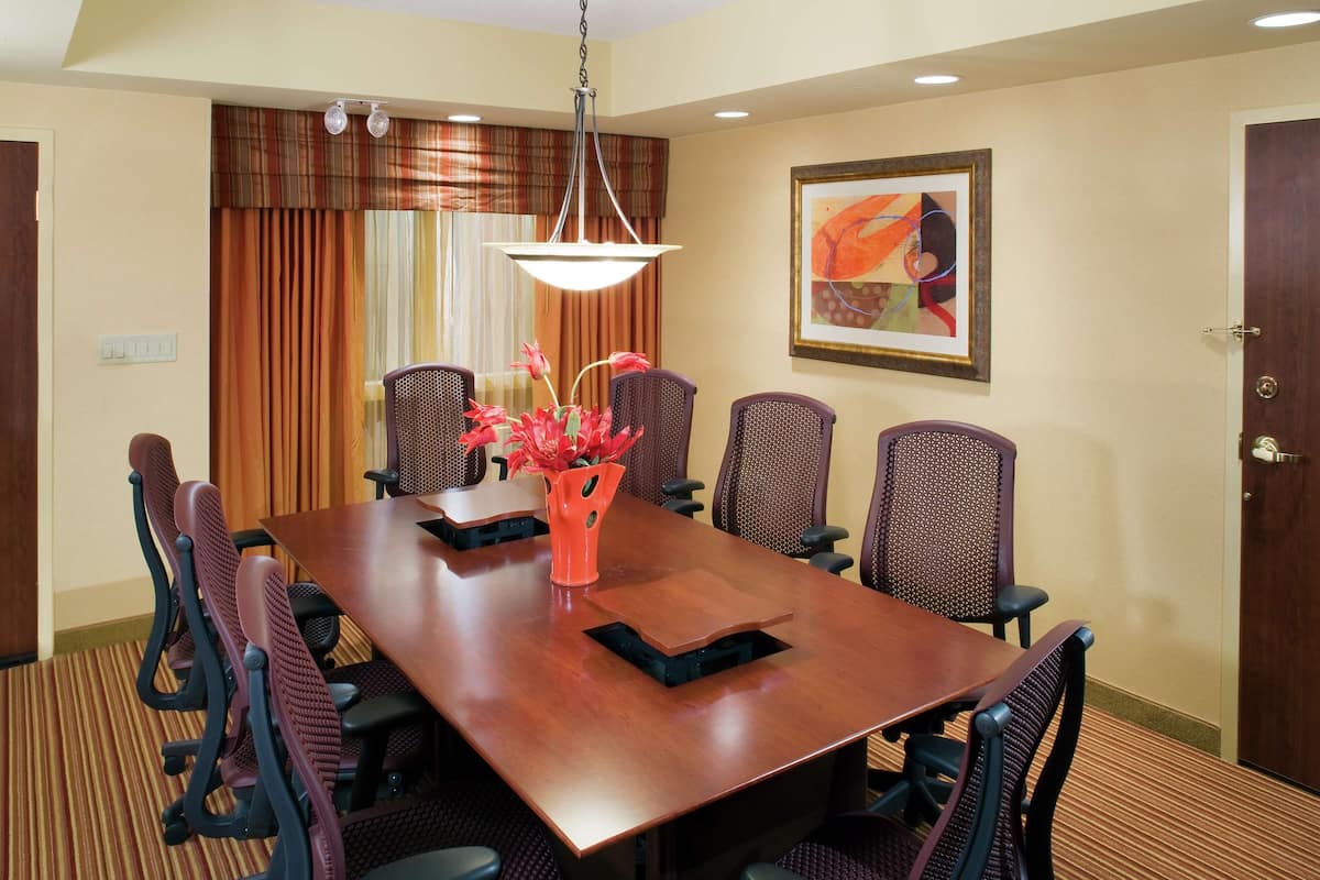 A conference room with a long wooden table, six chairs, a vase with flowers, and a painting on the wall.