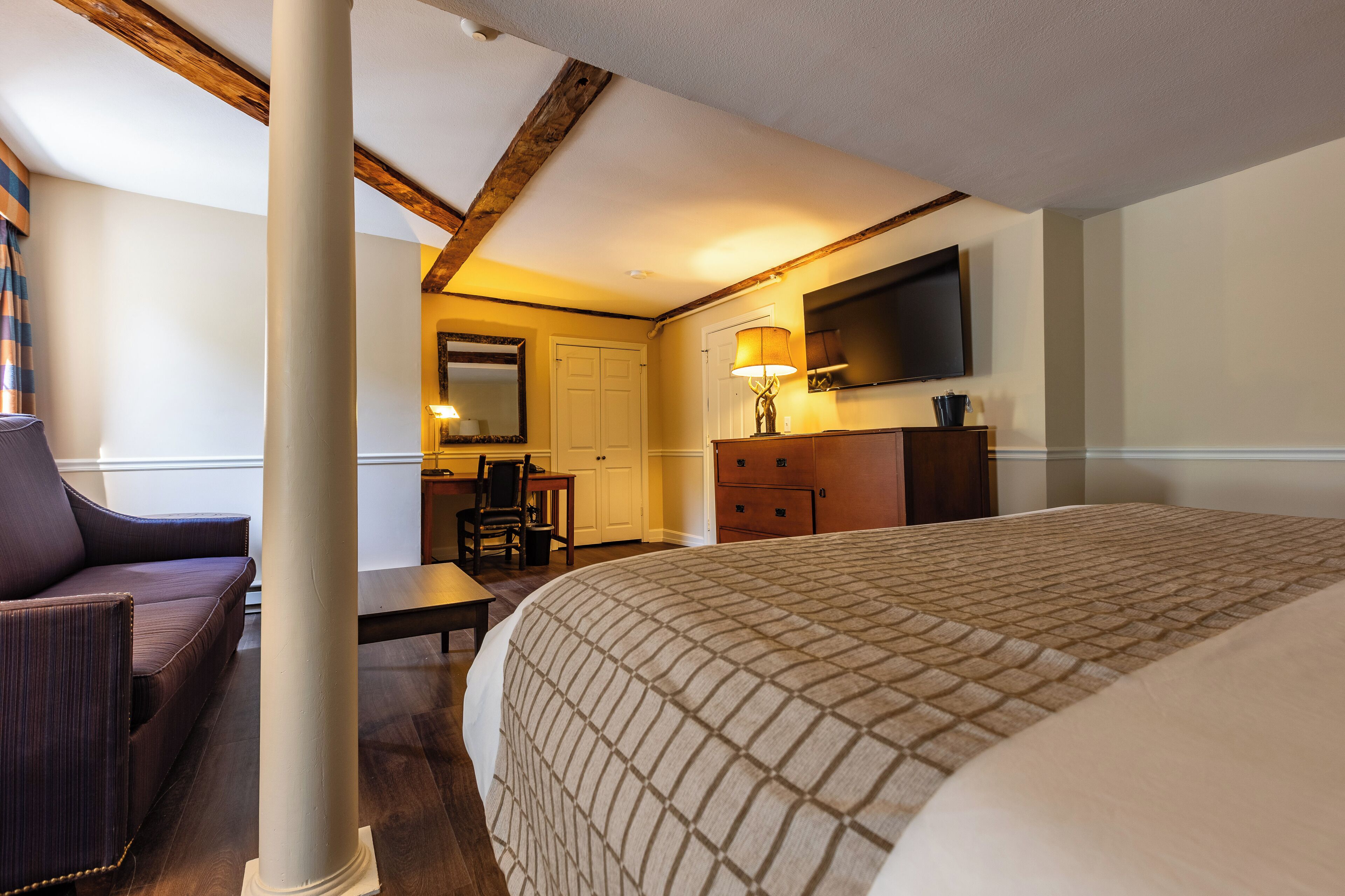 A hotel room with a bed, a desk, a chair, a dresser, and a television mounted on the wall.