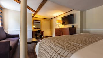 A hotel room with a bed, a desk, a chair, a dresser, and a television mounted on the wall.
