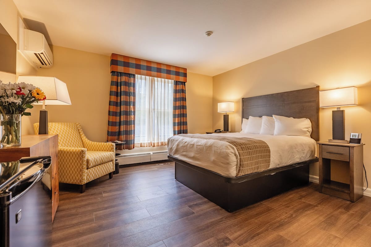 A hotel room with a bed, bedside lamps, a desk with a lamp, a chair, and a window with curtains.