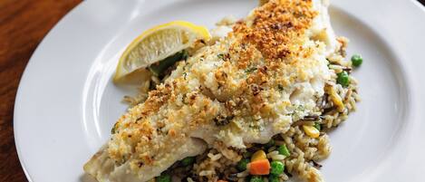 A plate of fish with rice and vegetables, a glass of white wine, and a glass of orange juice on a wooden table.